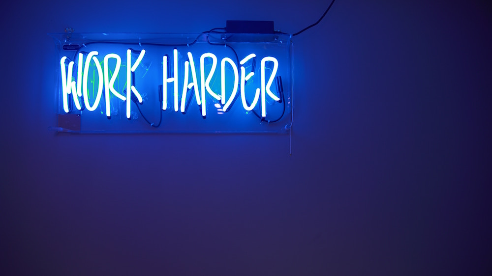 Blauer Hintergrund und weisse Leuchtschrift «Work harder»