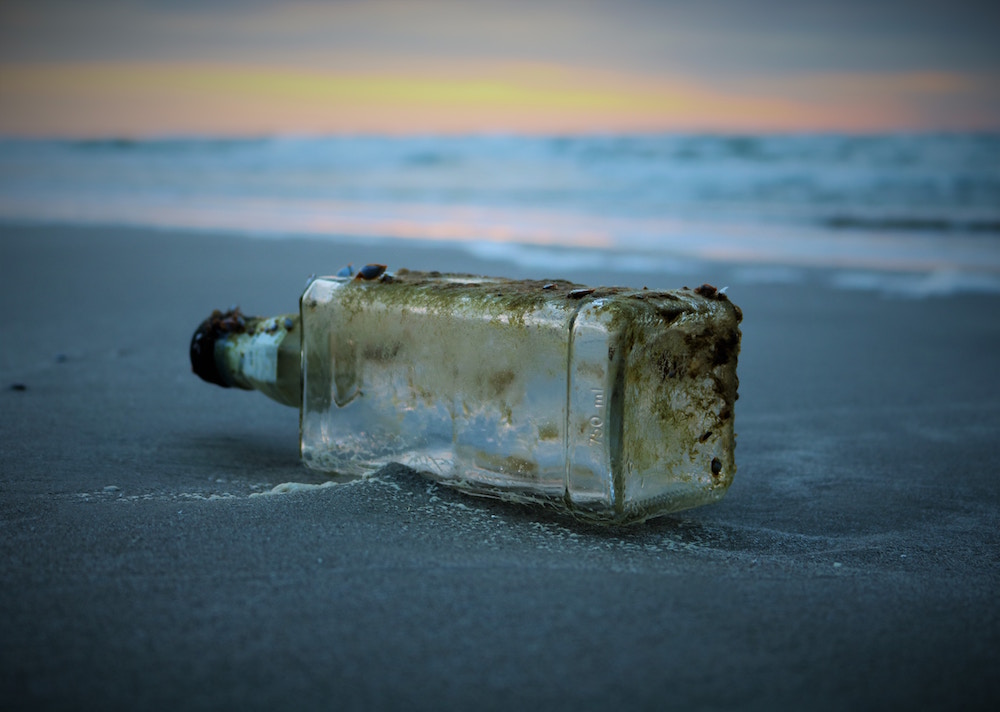 Leere PET-Flasche liegt am Meeresstrand bei Sonnenuntergang
