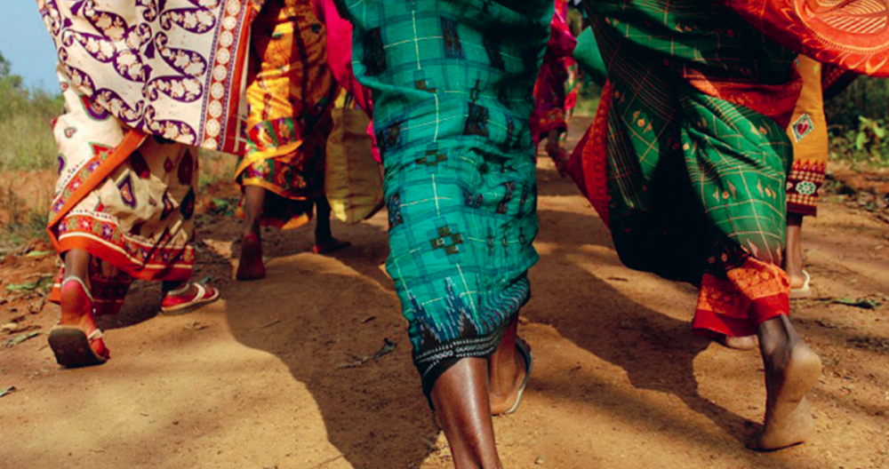 Nackte Füsse von marschierenden Menschen in Indien, die auf staubigem Boden gehen, mit bunter Kleidung