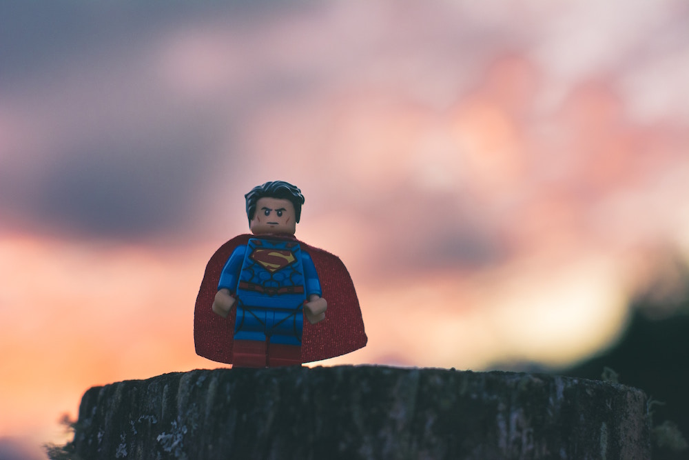 Playmobil-Figur von Superman mit wehendem Cape steht auf einem Felsen vor Sonnenuntergang und schaut grimmig