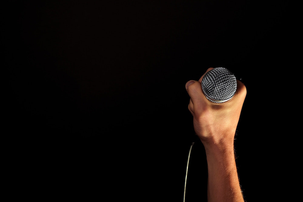 Männerhand vor einem schwarzen Hintergrund, die ein silbernes Mikrofon hält