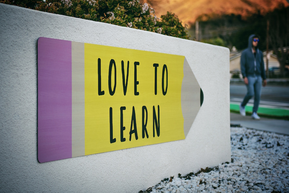 Ein aufgemalter Pfeil an einer weissen Wand, auf dem steht: Love to learn, und davor geht ein Jugendlicher