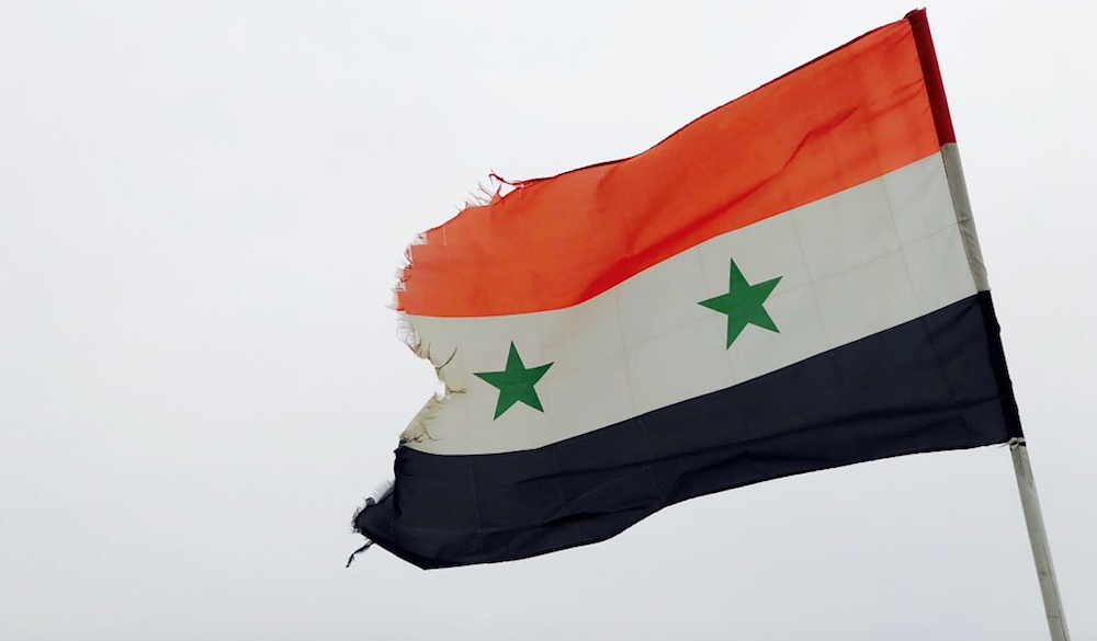 Flagge von Syrien rot-weiss-schwarz quer gestreift mit zwei grünen Sternen im mittleren weissen Drittel, die im Wind weht und links ausgefranst ist