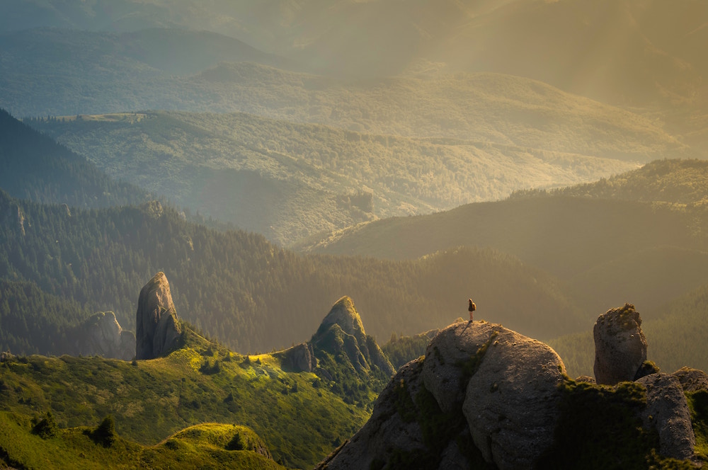 Panorama einer Hügellandschaft und ein kleiner Mensch, der auf einem Felsen steht und sie betrachtet