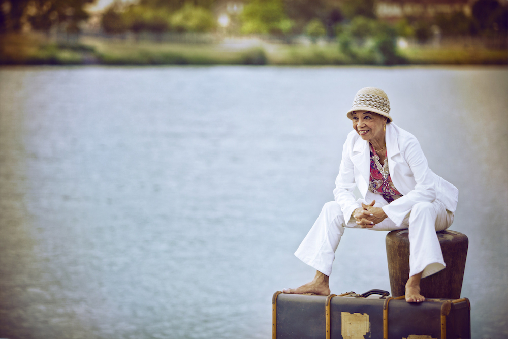 Die schwarze Jazz-Sängerin Othella Dallas sitzt auf einem Stein am See oder Meer und blickt in die Kamera
