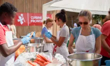 Mehrere Personen stehen draussen um einen Tisch und kochen gemeinsam