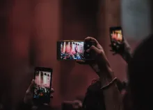 Drei Hände halten drei Smartphones in die Luft vor dunklem Hintergrund