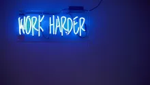 Blauer Hintergrund und weisse Leuchtschrift «Work harder»